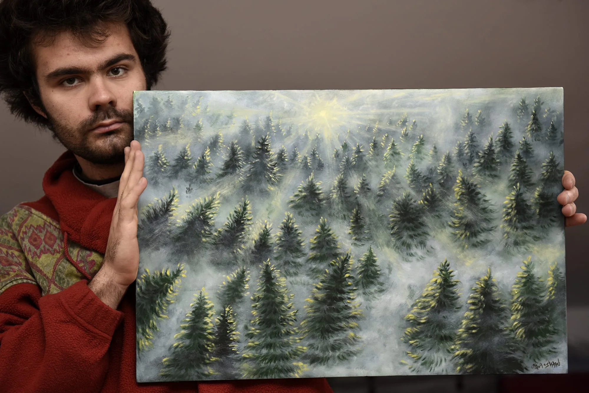 Lorenzo Forti tiene in mano un suo quadro di foresta nella nebbia